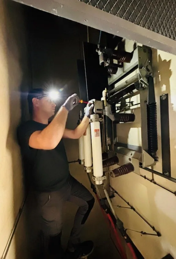 Electricista realizando mantenimiento en celda de media tensión con linterna
