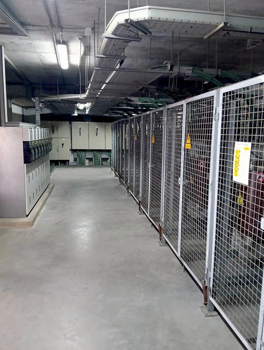 Vista general de sala de centro de transformación con celdas de media tensión, transformadores en jaula metálica y bandejas de cables verdes